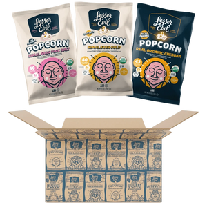 Three bags from the LesserEvil Snacks Popcorn Best Sellers Box—featuring Himalayan Pink Salt, Real Organic Cheddar, and Himalayan Gold popcorn—above an open box of neatly arranged bags.
