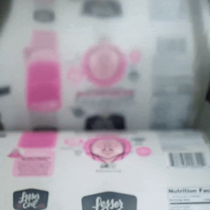 A roll of food packaging labels moves through a printer, showing a pink smiling face and the words “Lesser Evil” and “Lessen the Evil.”.