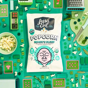 A Flavor-FULL Snacks Box by LesserEvil Snacks sits among popcorn, game tiles, herbs, and Intergalactic Onion Moonions on a vibrant green background.