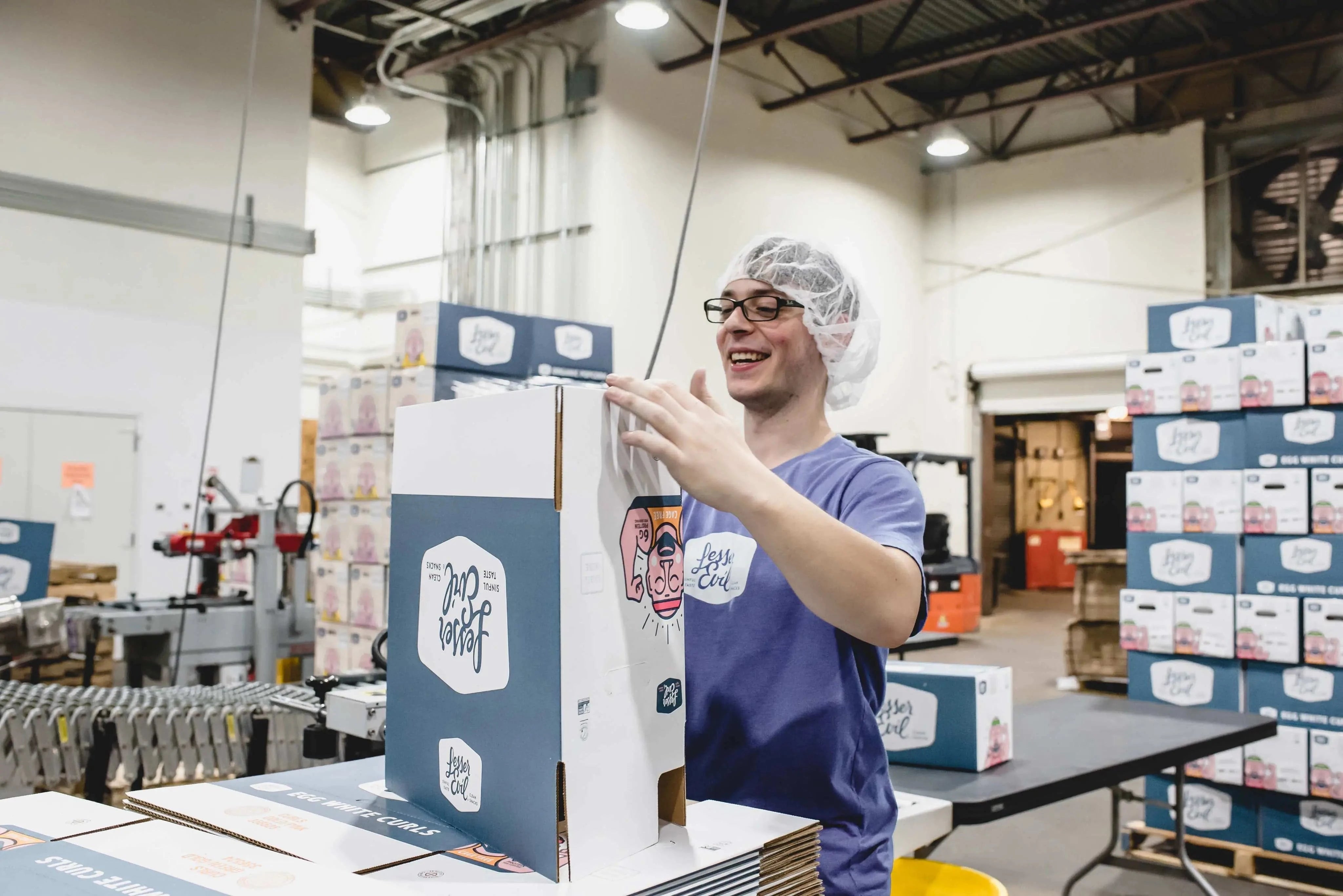 LesserEvil warehouse employee smiles while assembling a box for healthy organic snacks.
