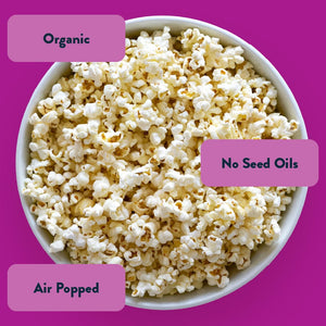 A bowl of LesserEvil Snacks' 24 Pack Snack Size Halloween Himalayan Pink Organic Popcorn sits on purple, labeled Organic, Air Popped & No Seed Oils—perfect for snack-sized bags!.