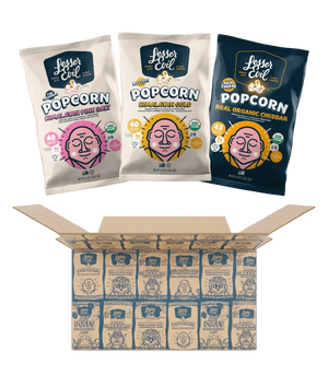Three bags from the LesserEvil Snacks Popcorn Best Sellers Box—featuring Himalayan Pink Salt, Real Organic Cheddar, and Himalayan Gold popcorn—above an open box of neatly arranged bags.