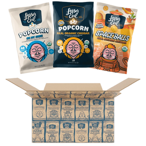 Three bags of LesserEvil Snacks, including Cheddar Space Balls and Oh My Ghee Popcorn, sit above an open Dairy Good Snacks Box filled with assorted snack bags.