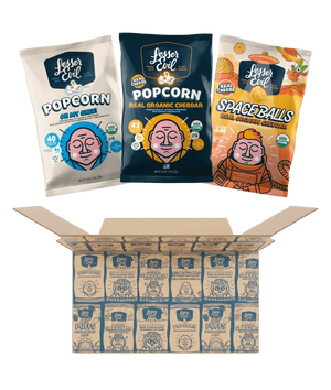 Three bags of LesserEvil Snacks, including Cheddar Space Balls and Oh My Ghee Popcorn, sit above an open Dairy Good Snacks Box filled with assorted snack bags.