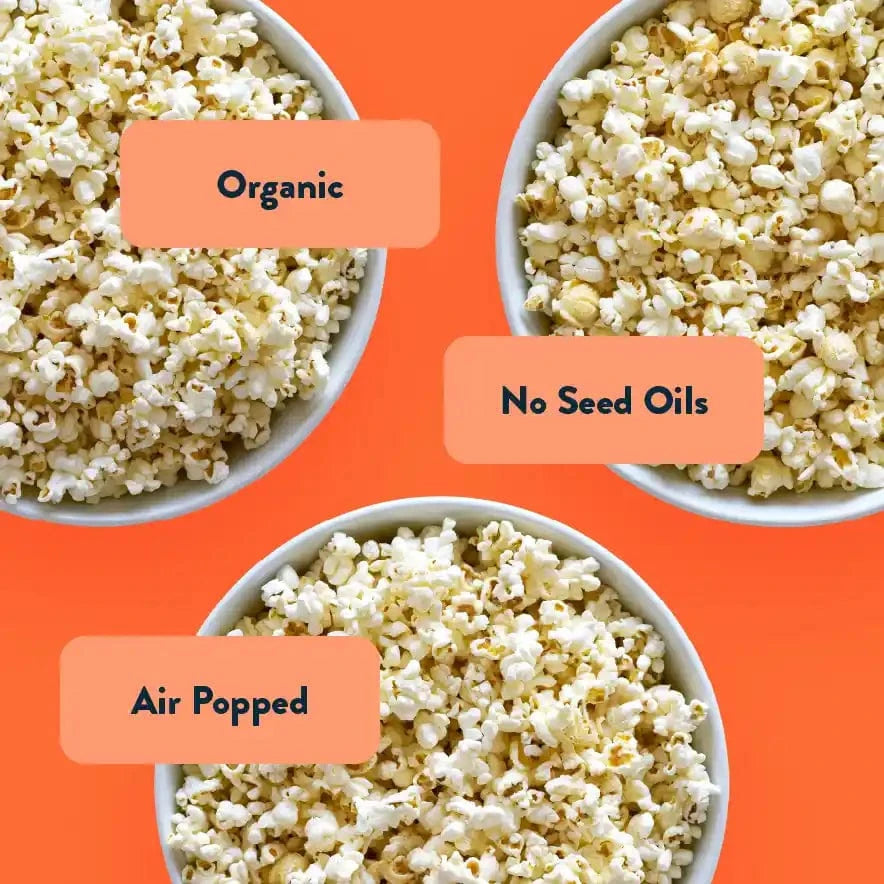 Three bowls of popcorn on orange background labeled Organic, White Cheddar, and Air Popped from The Classics Popcorn Box by LesserEvil Snacks.