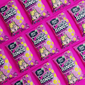 Several pink bags of LesserEvil Berry Blast Cosmic Rings cereal, with kid-friendly cartoon packaging and colorful ring shapes, are displayed in a diagonal pattern.