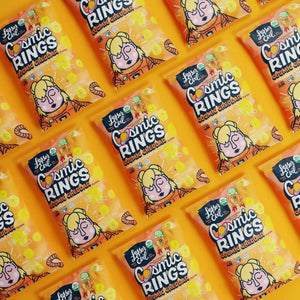 Rows of bright orange LesserEvil Cosmic Cheddar Cosmic Rings vegan snack bags with cartoons are neatly arranged in a repeating pattern.