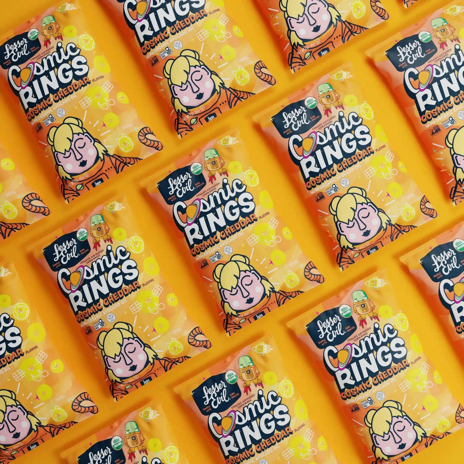 Rows of bright orange LesserEvil Cosmic Cheddar Cosmic Rings vegan snack bags with cartoons are neatly arranged in a repeating pattern.