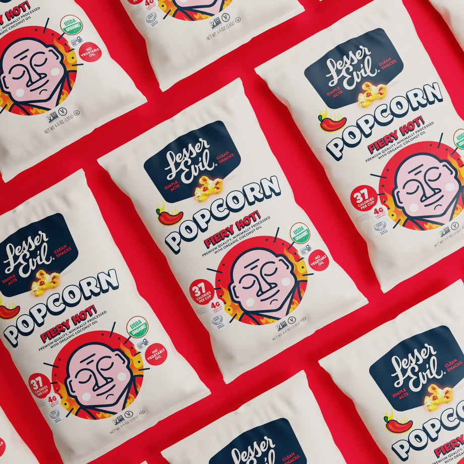 LesserEvil Fiery Hot Organic Popcorn bags are arranged diagonally on a bright red background.