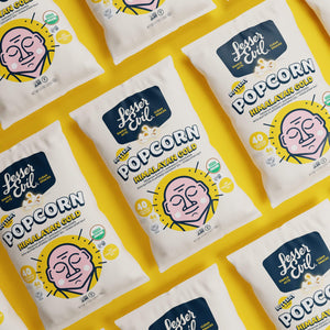 Multiple bags of LesserEvil Himalayan Gold Organic Butter Flavor Popcorn are arranged diagonally on a bright yellow background.