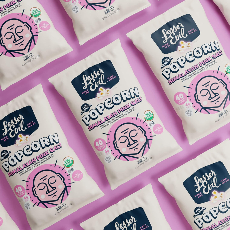 OrganicPopcorn Himalayan Pink Salt Organic Popcorn bags, with a stylized face design, are neatly arranged on a pink background.