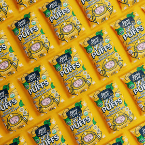 Bright yellow bags of LesserEvil Broccoli Cheddar Blast Lil Puffs, featuring cartoon astronauts and broccoli, arranged in a diagonal repeating pattern.