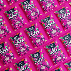 Multiple packs of LesserEvil Star-Berry Beet Lil Puffs, a berrylicious treat with 0g added sugar, in vibrant cartoon packaging on a matching pink background.