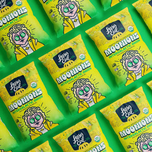 Rows of bright green bags of LesserEvil Intergalactic Onion Moonions, featuring a cartoon in green glasses and a yellow jacket, arranged diagonally.