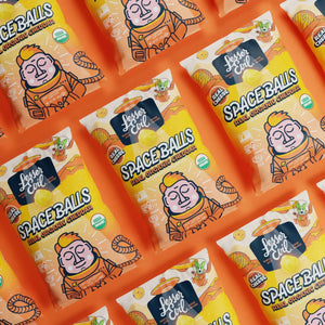Several bags of SpaceBalls Real Organic Cheddar Space Balls are neatly arranged in a colorful pattern against an orange background.