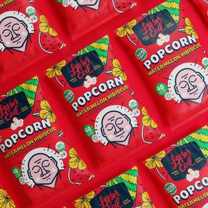 Multiple red bags of LesserEvil Watermelon Hibiscus Popcorn, featuring cheerful faces and summery watermelon and hibiscus designs in a vibrant arrangement.