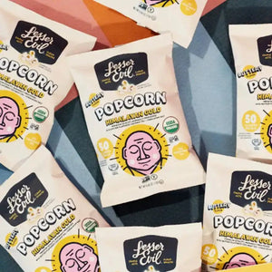 Himalayan Gold Organic Popcorn – 24 Pack by LesserEvil Snacks is displayed on a colorful geometric background with bold black and yellow text and a pink-faced cartoon.