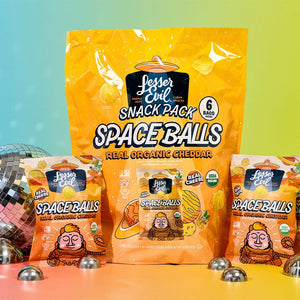 The SpaceBalls Real Organic Cheddar Space Balls Snack Pack is shown with a large bag and three small bags on a colorful background with metal balls and a disco ball.