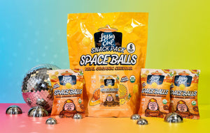The SpaceBalls Real Organic Cheddar Space Balls Snack Pack is shown with a large bag and three small bags on a colorful background with metal balls and a disco ball.