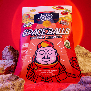 A bag of SpaceBalls Buffalo Cheddar Space Balls stands among rocks, with a cartoon astronaut on bold red-orange packaging and a glowing red background.