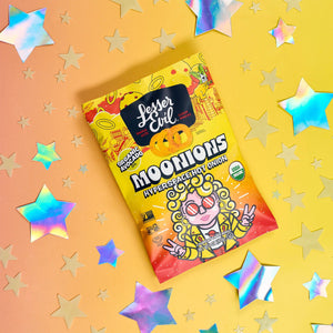 A Little Spice Snacks Box by LesserEvil Snacks sits on a yellow-orange background with shiny holographic stars scattered around.