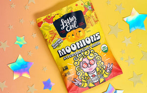 A vibrant bag of LesserEvil Hyperspace Hot Onion Moonions shows a curly-haired cartoon astronaut with sunglasses on a yellow-orange background with shiny stars.