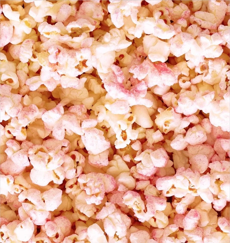 Close-up of popcorn coated with light pink and white seasoning, creating a colorful and textured surface.