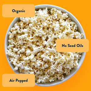 A white bowl of OrganicPopcorn Real Organic Cheddar Popcorn on yellow background, labeled: Organic, Air Popped, No Seed Oils.