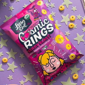 A pink bag of LesserEvil Berry Blast Cosmic Rings cereal, made with organic fruit powders, rests on a purple surface with scattered rings and glow-in-the-dark stars.