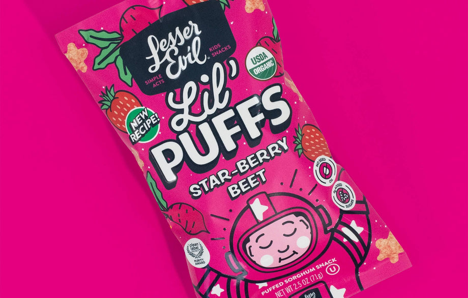 A bright pink bag of LesserEvil Star-Berry Beet Lil Puffs, a berrylicious snack with 0g added sugar, cartoon astronaut, and USDA Organic and New Recipe labels.