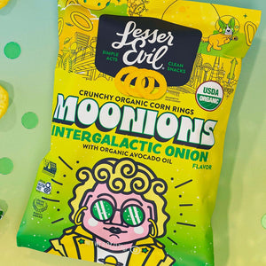 A brightly colored bag of LesserEvil Intergalactic Onion Moonions sits on a table with onion snacks and disco balls, made with clean ingredients.
