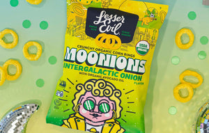 A brightly colored bag of LesserEvil Intergalactic Onion Moonions sits on a table with onion snacks and disco balls, made with clean ingredients.